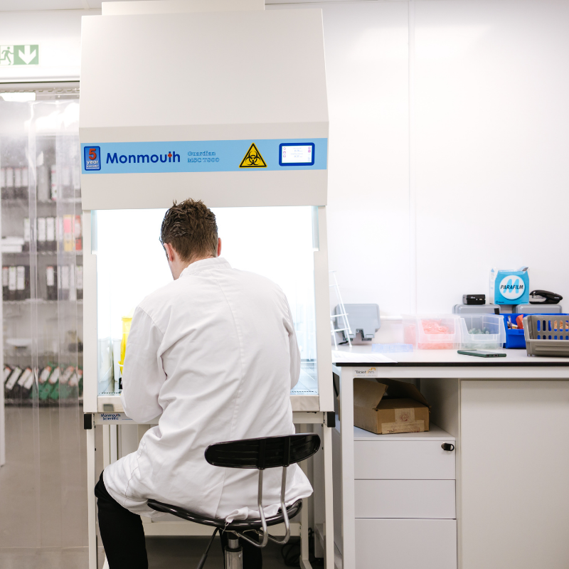 Person in a lab coat working at a desk with in a laboratory setting.